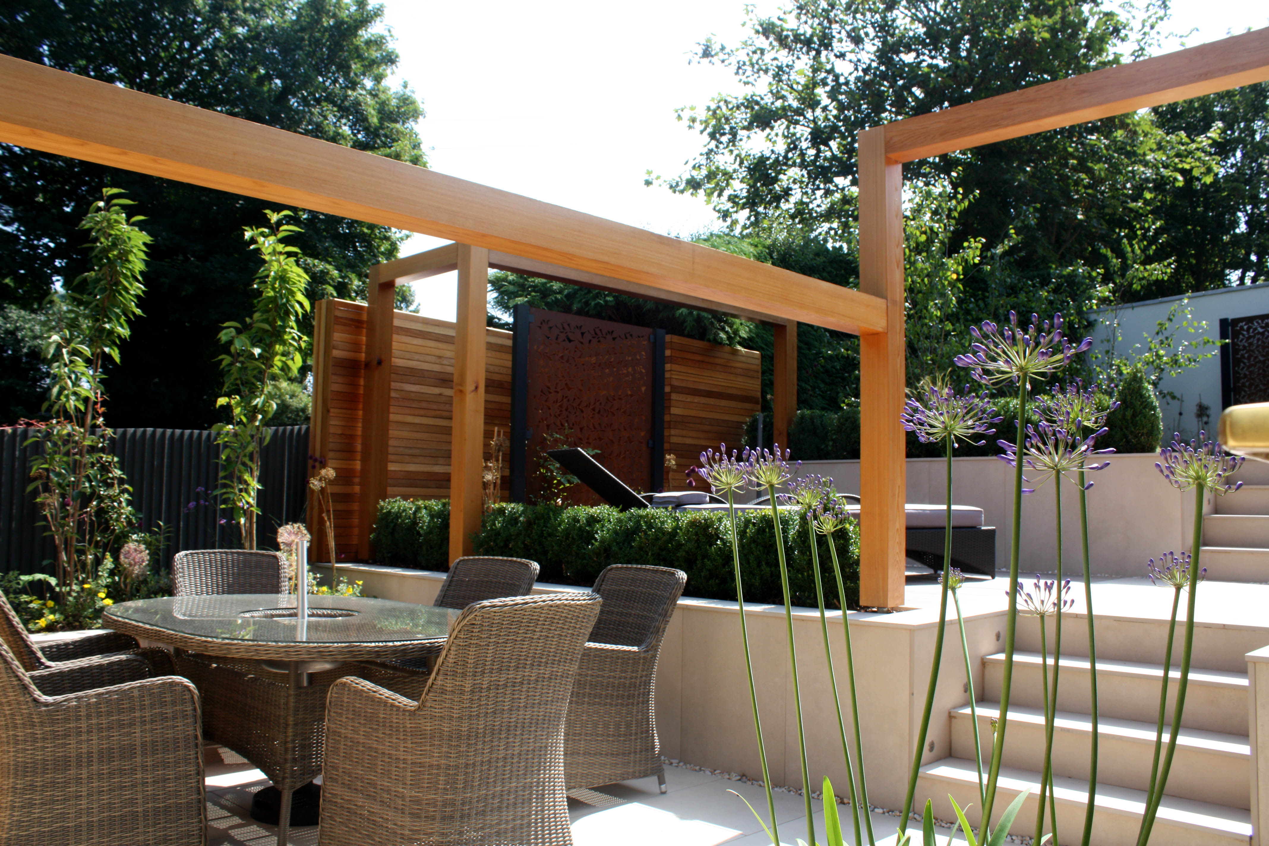 lower area of contemporary garden with agapanthus flowers and rattan chairs and table by steps